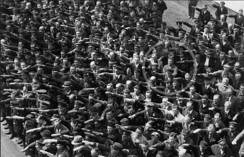 1936 Almanyası‘ndan siyah beyaz bir fotoğraf. Fotoğrafta coşkulu bir kalabalık var. Hepsi de parmaklarını birleştirdikleri sağ ellerini ileriye doğru uzatmışlar ve Nazi selamı veriyorlar. Ve o insan selinin ortasında bir kişi, sadece bir kişi kollarını kavuşturarak oturuyor. Nazi selamı vermeyi reddeden o adamın adı August Landmesser.